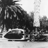 This photo, found in the Airstream corporate archives, depicts an early Airstream trailer, probably circa 1933. Although the man is not identified, it appears to be Wally Byam. The early Airstream trailers used this ‘teardrop’ design for aerodynamic efficiency. The sleeping compartment was towards the rear of the trailer. There appears to be someone sitting inside the trailer.