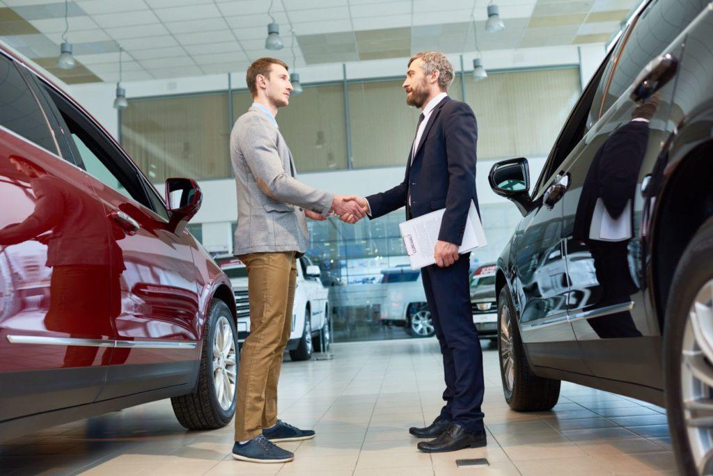 Sales consultant and a customer at a car dealership. Our recommendation is to ask politely for the invoice price as part of the negotiation process.