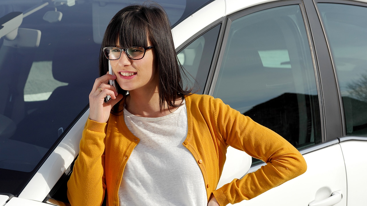 beautiful young brunette woman on the phone against her car
