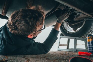 a mechanic wearing glasses and blue coveralls installs a new component after a catalytic converter theft