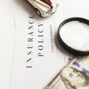 featured image that contains a white document labeled insurance policy, a $100 bill, and a magnifiying glass