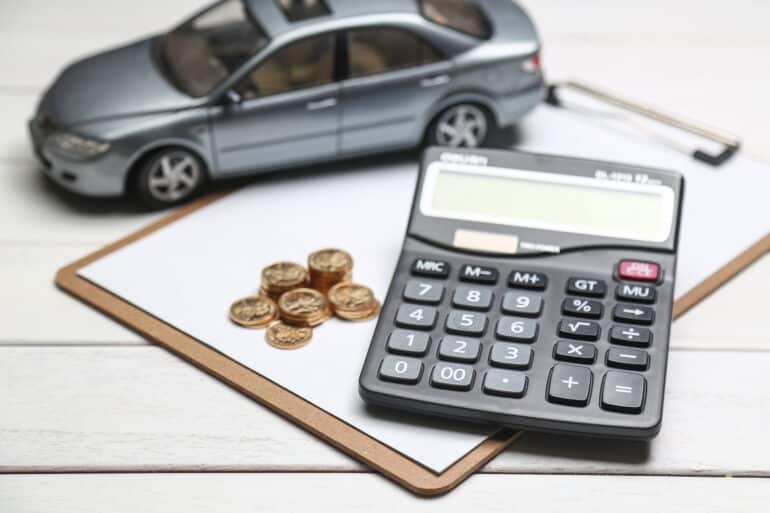 an image showing a calculator, a stack of coins, a model car, and a clipboard on a table
