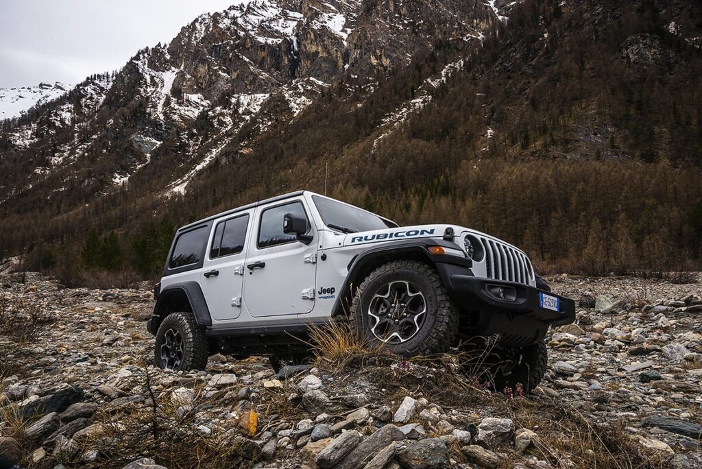 a jeep wrangler 4xe climbs over rocky terrain with mountains in the background