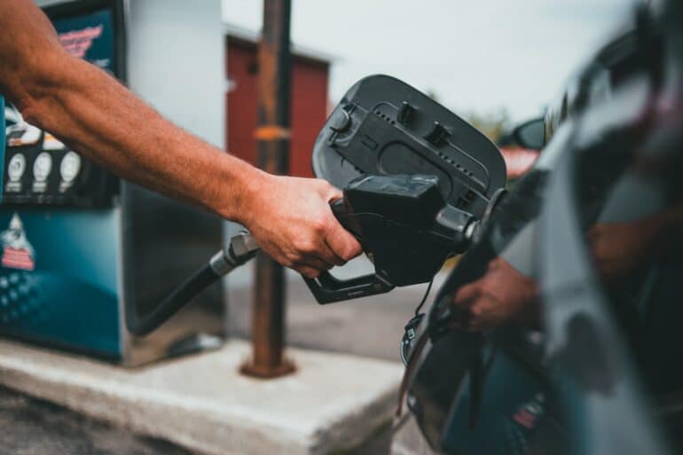 a person's arm holds the nozzle of a gas pump as it is filling up the tank of a car