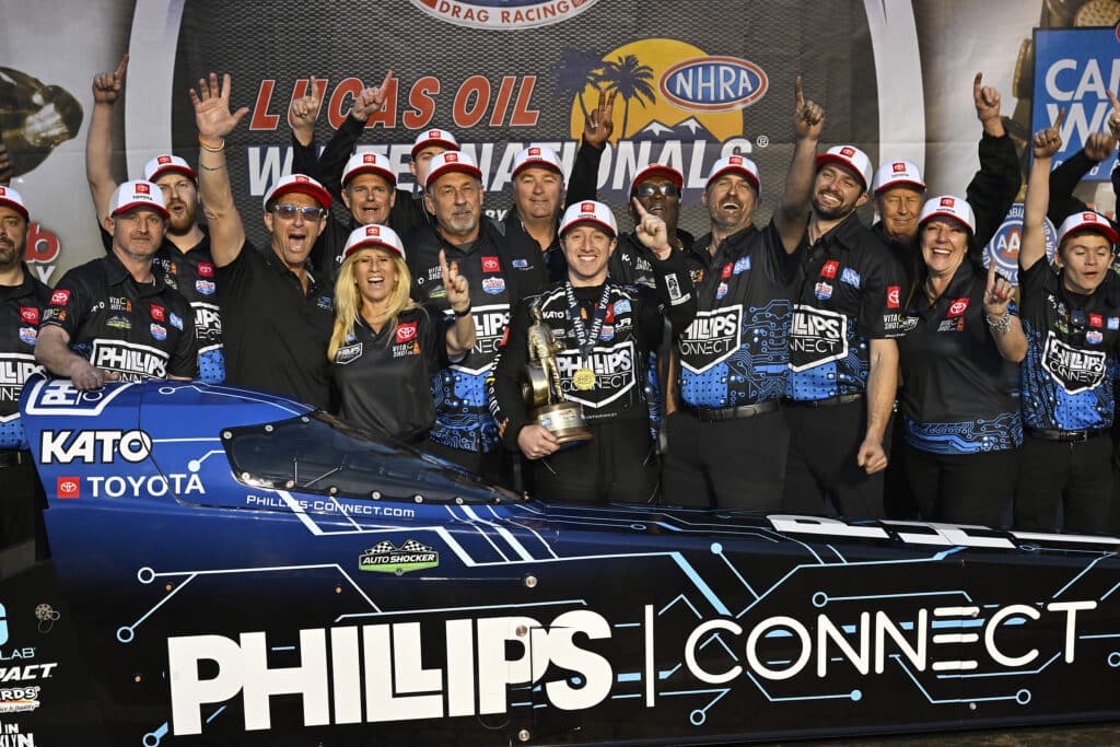 Justin Ashley and his team standing behind his Top Fuel dragster celebrating a win at the 2022 Winternationals