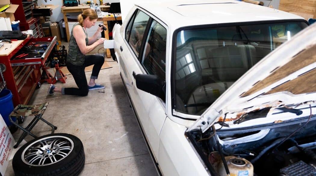 anna hursley works on her 1988 white bmw in the back of her garage