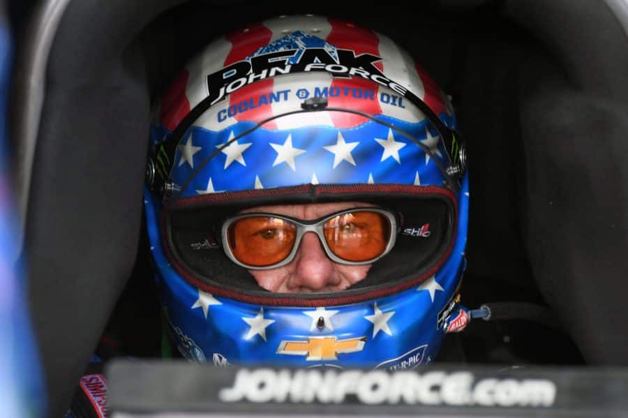 john force sitting in a dragster with his american flag helmet on