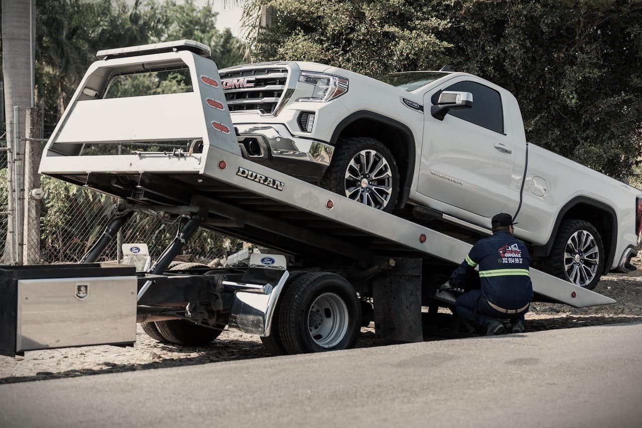 a white pickup truck being loaded onto a flatbed tow truck for auto loan debt delinquency